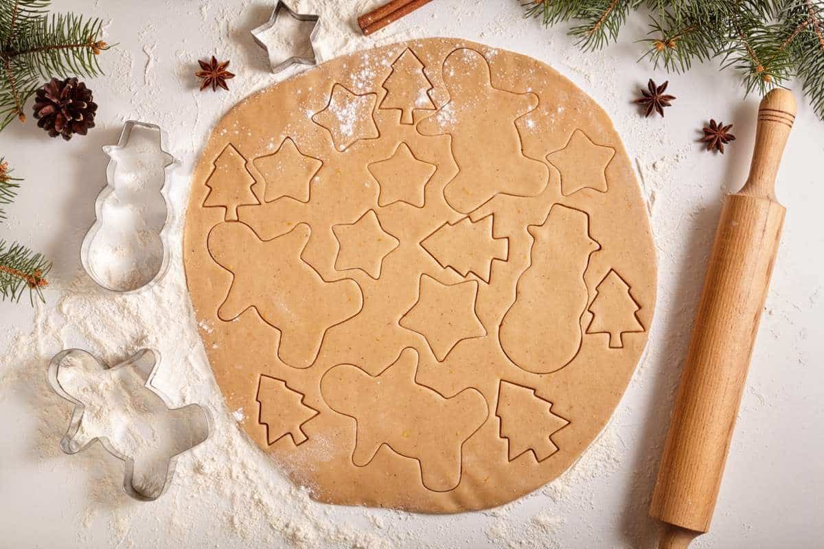 Gingerbread cookies dough preparation recipe with man shape, fir trees, snowman and star forms, cinnamon rolling pin, flour on white kitchen table. Traditional homemade christmas dessert